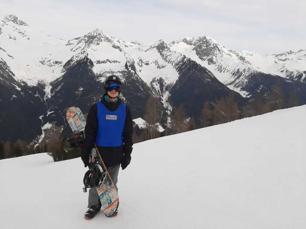 Ein Snowboarder steht mit dem Brett vor verschneiten Berggipfeln.